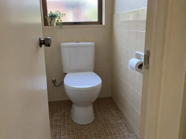 Clean white toilet in a tiled small bathroom with a frosted window in Prairiewood