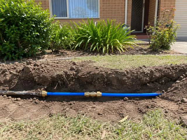 Exposed repaired water pipe in a front yard trench beside a brick house in Smithfield