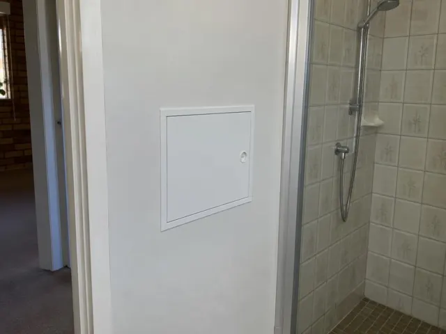 Small access panel in a white wall beside a tiled shower in a home interior in Greystanes